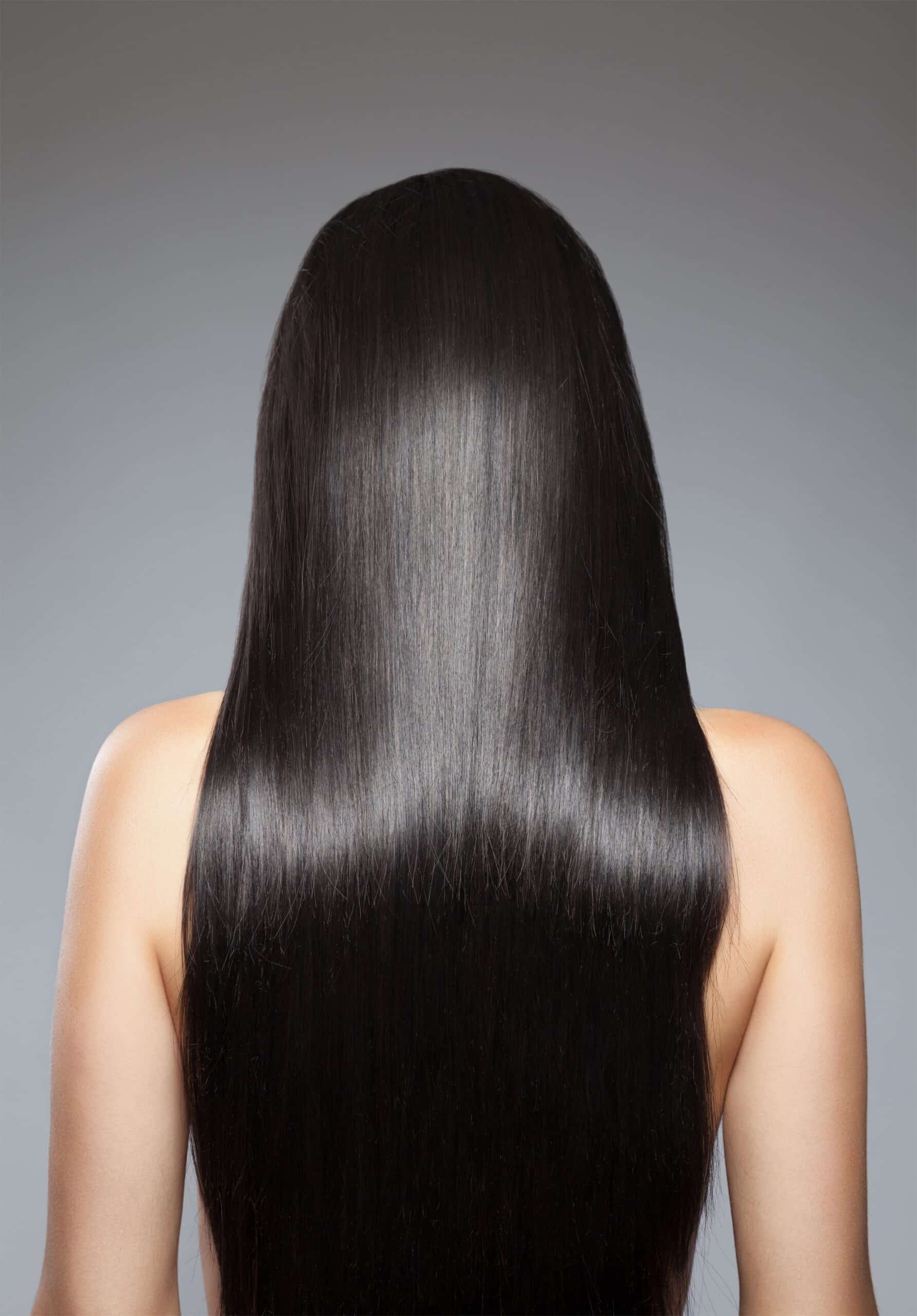 A close-up view of long, straight black hair from behind, with a smooth and shiny texture, set against a neutral gray background.