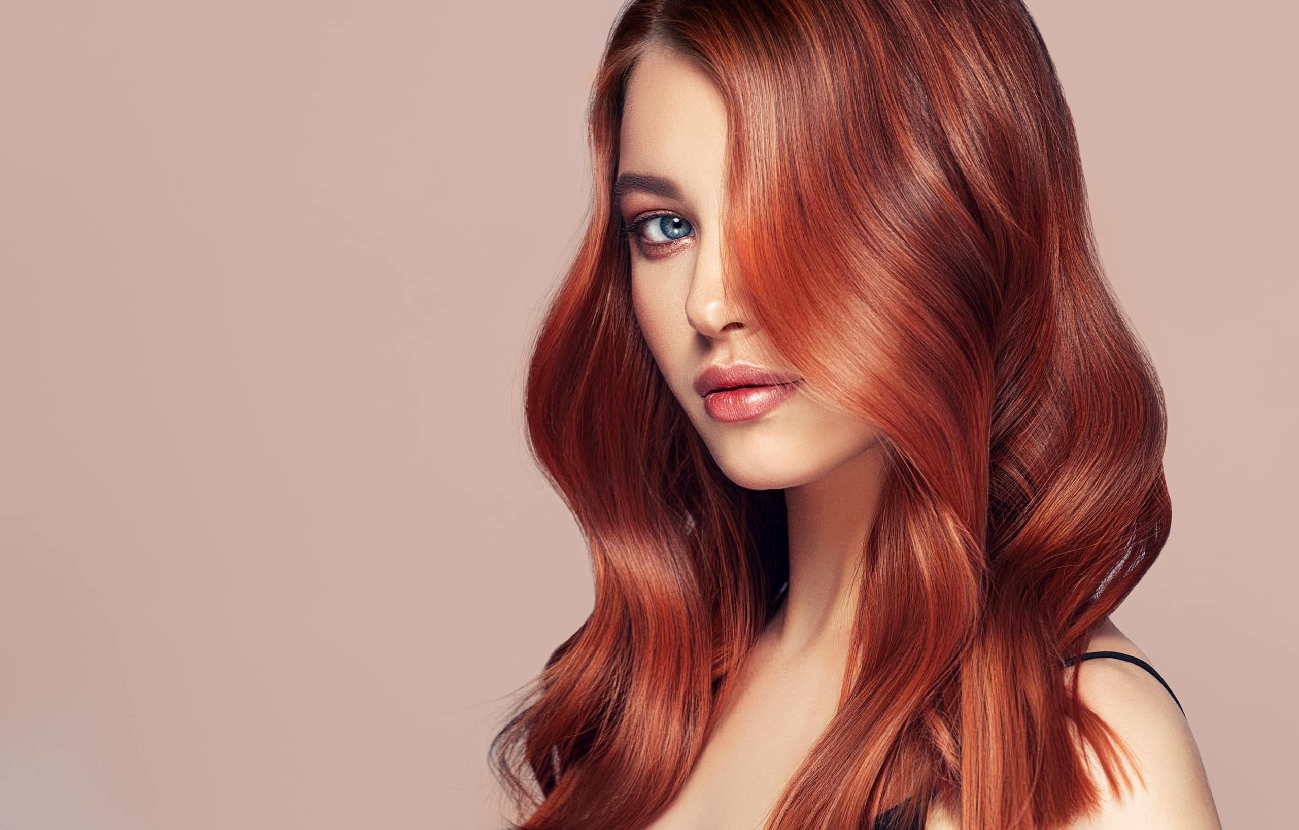 A woman with long, wavy auburn hair and blue eyes poses with a soft expression against a neutral background, highlighting her features.