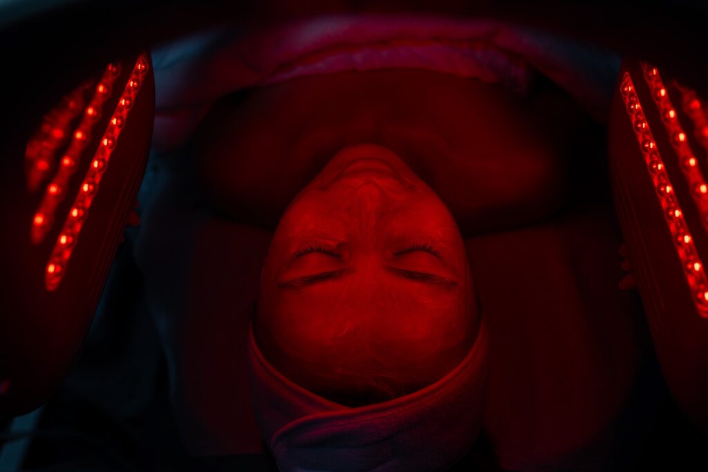 What Is Infrared Therapy? The Science and Your Options at Elevate Med Spa - Elevate Med Spa A person lying down under red light therapy devices, with a calm expression. The setting is dimly lit, highlighting the red lights on both sides of the face.