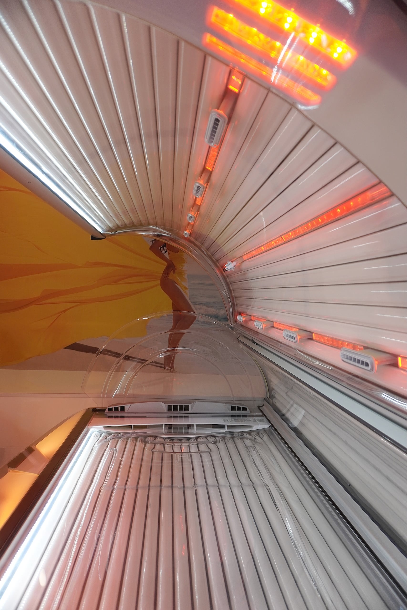 Inside view of a tanning bed showing the curved configuration of the UV lamps and reflectors. The interior is illuminated with red lights, enhancing the visual effect of the tanning environment, with a sleek modern design.