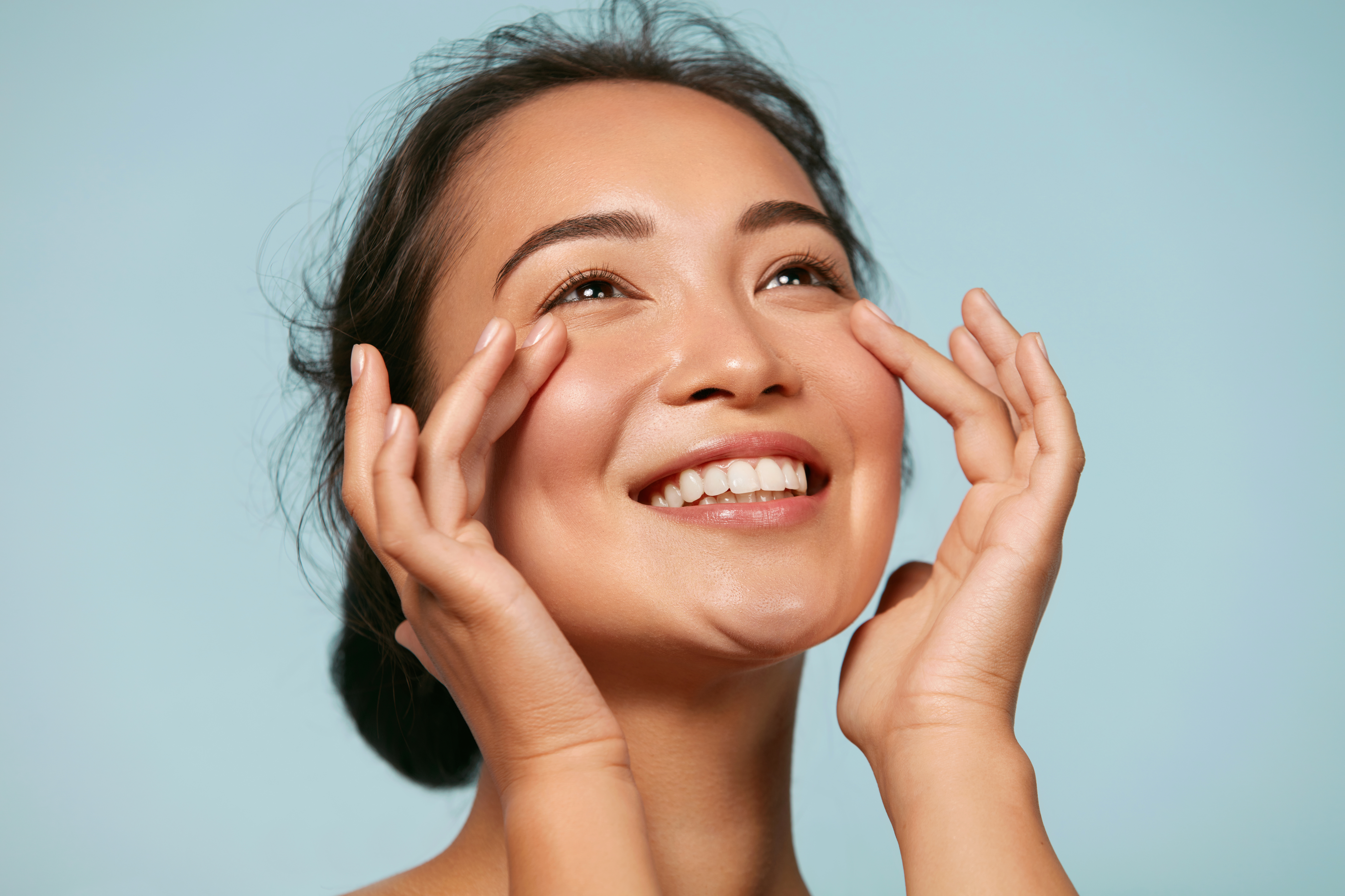 A smiling woman with her hands near her face against a light blue background.